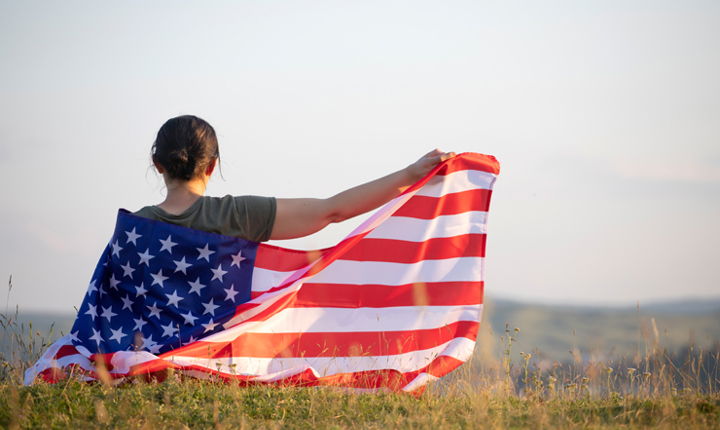 Mujer de espaldas estirando una bandera de EEUU sobre su espalda