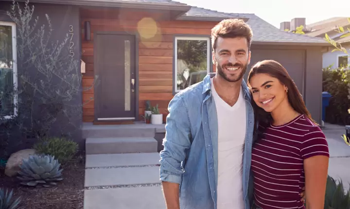 Pareja joven de hombre y mujer sonriendo afuera de su casa