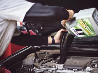 Persona cambiando el aceite de su automóvil en el garaje usando soportes de seguridad, recipiente de drenaje y herramientas adecuadas para realizar el mantenimiento de forma segura y responsable.